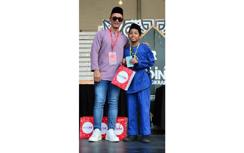 Salah seorang kanak-kanak menerima sumbangan Aidilfitri redONE Mobile yang disampaikan oleh Jemay (kiri).