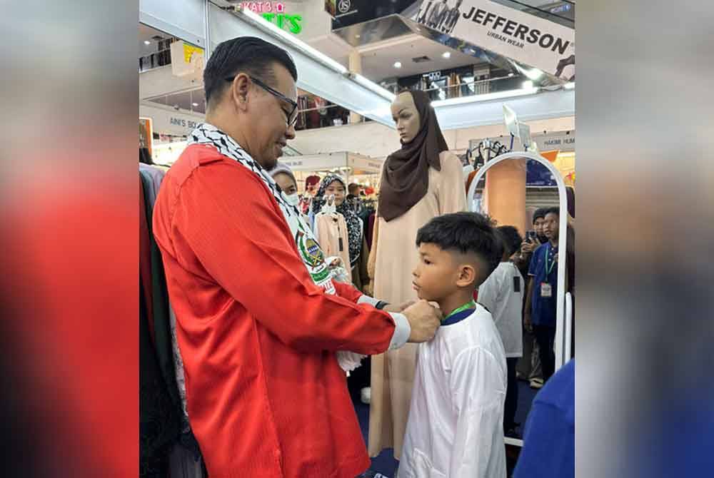 Muhammad Azki membantu seorang kanak-kanak mencuba baju raya baharu.