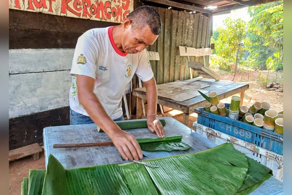 Fauzi memasukkan daun pisang hutan ke dalam buluh.