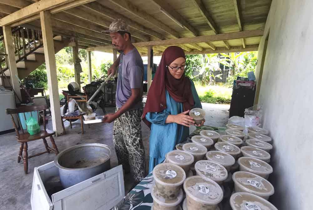 Masliana membungkus bubur lambuk sementara Hasimie mencedok juadah itu daripada periuk yang dimasak di Kampung Losong Lebai Salleh, Kuala Terengganu.