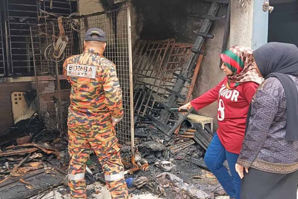 Faridah (dua kanan) menunjukkan kesan kebakaran ketika anggota bomba menjalankan siasatan dan kerja-kerja forensik di rumahnya di Taman Scientex, Pasir Gudang pada Ahad.