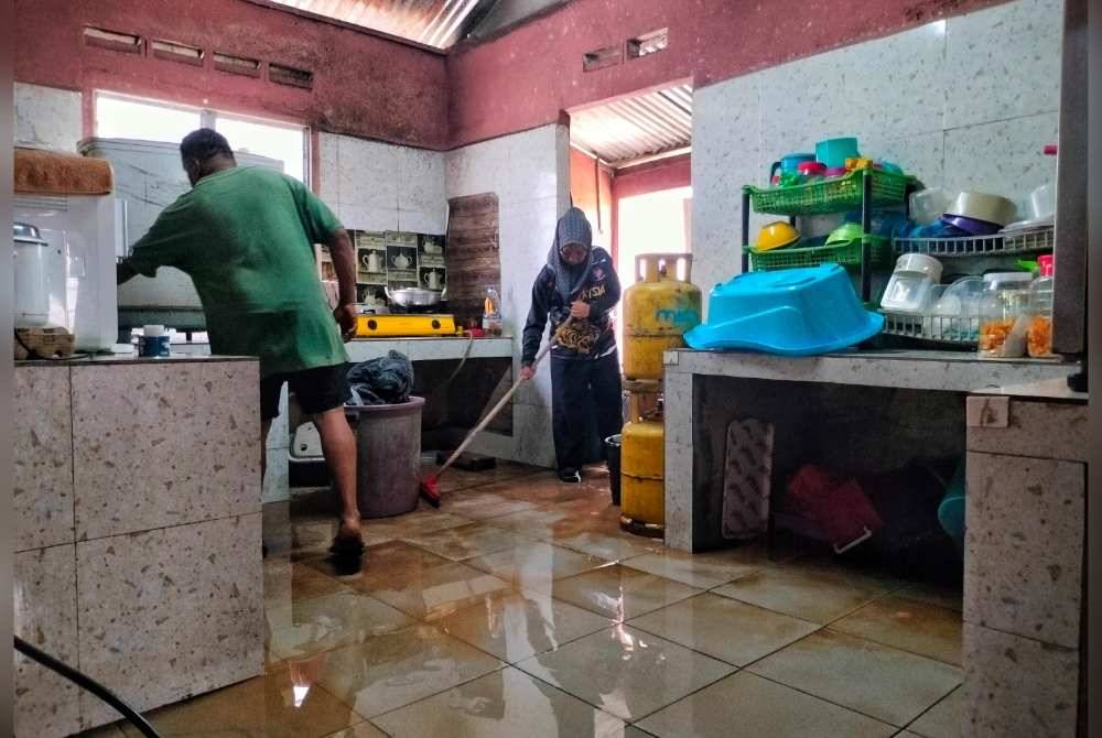 Fauziah dan suaminya mencuci lantai dapur yang diselaputi lumpur.