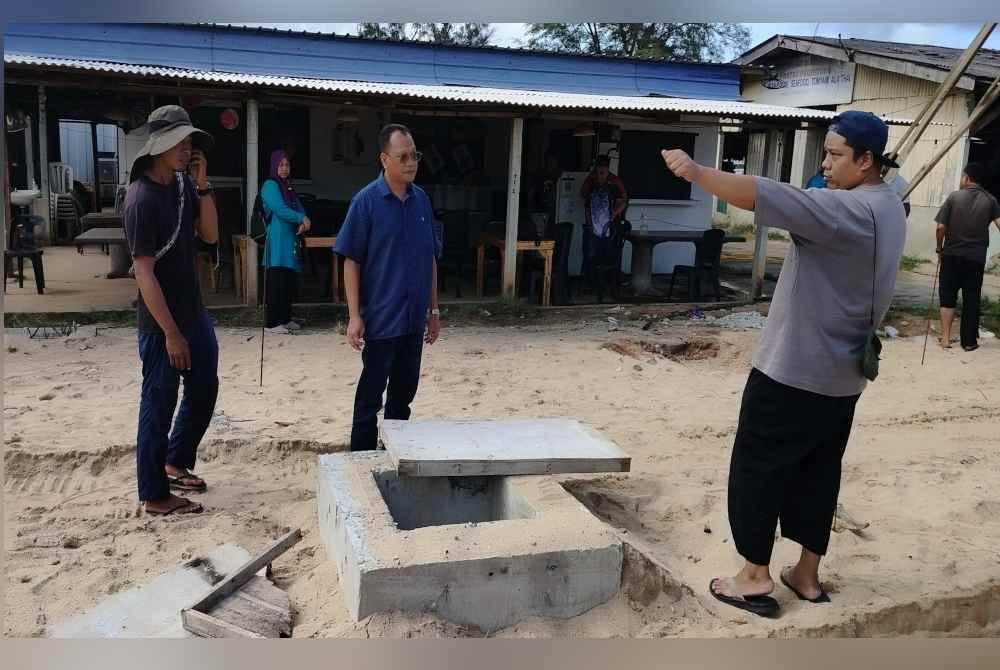 Mohd Fairus (kanan) menunjukkan kepada Andansura (tengah) kerja-kerja pembinaan longkang mengatasi banjir kilat yang sedang dijalankan di hadapan kedainya di Pantai Pelindung di sini.