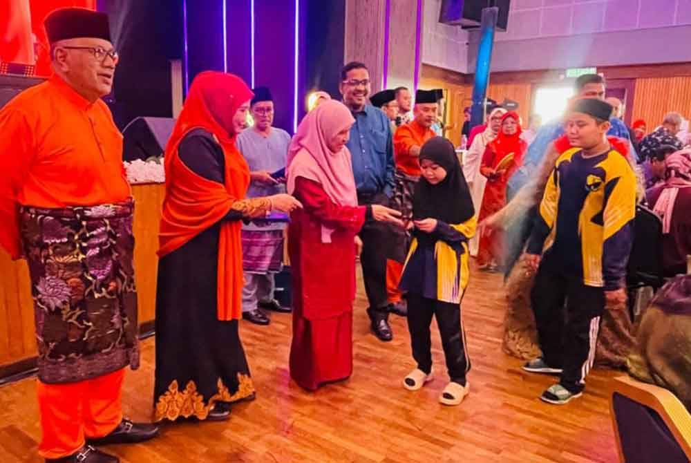 Mohd Zolkafly (kiri) mengiringi isteri Menteri Besar Perak, Datin Seri Aezer Zubin menyampaikan duit raya kepada kanak-kanak yang hadir sempena Rumah Terbuka Aidilfitri di Pusat Konvensyen Sungai Siput pada Khamis.