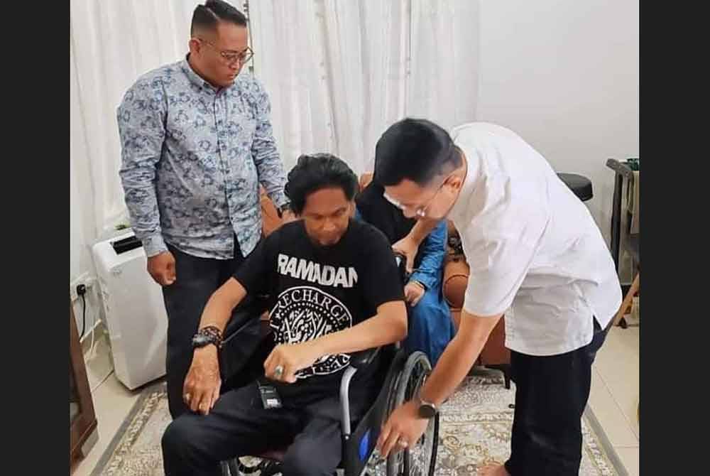 Borhan (kanan) ketika menyerahkan sumbangan kerusi roda kepada Ali (tengah) di kediaman penyanyi itu di Salak Tinggi.