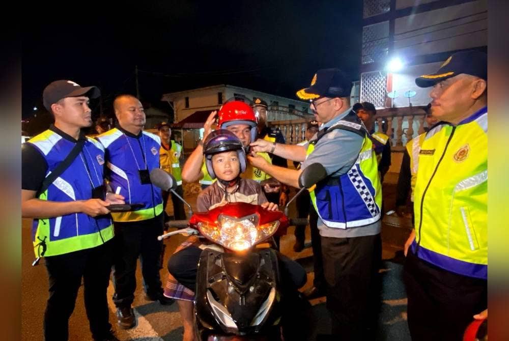 Mohd Misuari (dua dari kanan) memakaikan topi keledar baharu kepada pengguna jalan raya terpilih semasa Operasi Penguatkuasaan Perayaan HRA 2024 di Akademi Pengangkutan Jalan Wilayah Timur di Kota Bharu pada Khamis.