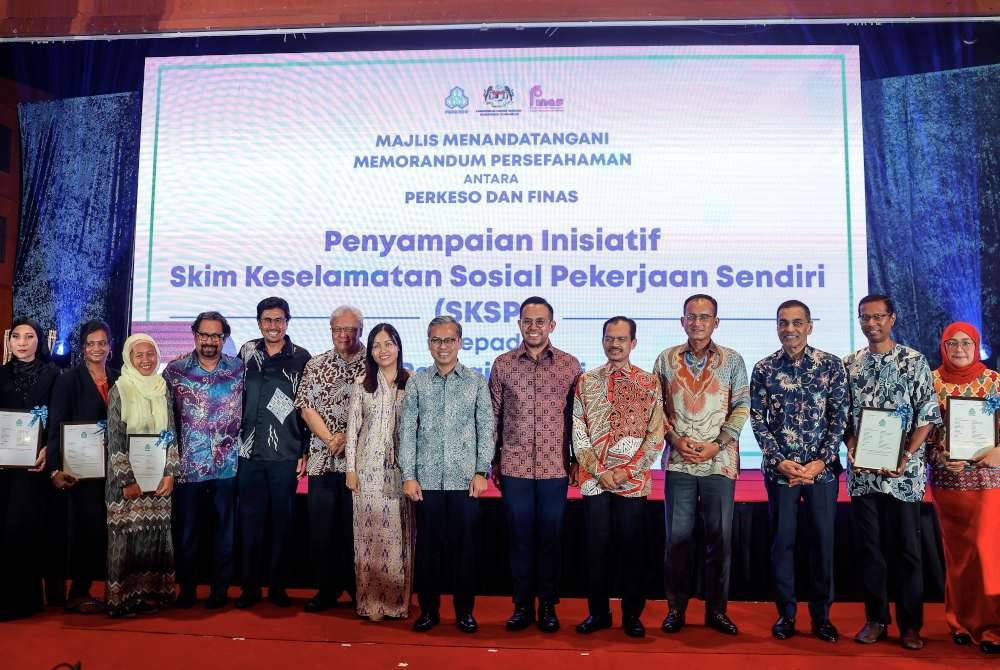 Fahmi (tengah) bersama Steven (enam, kanan) bergambar bersama para penerima inisiatif Skim Keselamatan Sosial Pekerjaan Sendiri pada Majlis Menandatangani Memorandum Persefahaman antara Perkeso dan Finas pada Selasa. Foto Bernama