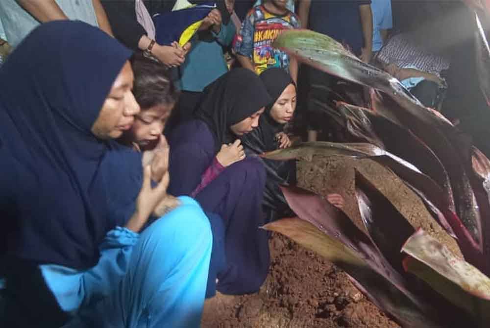 Nur Qistina (dua kiri) membaca doa untuk arwah ibunya di di Tanah Perkuburan Islam Masjid Haji Nyak Gam, Kampung Ruat, di sini.