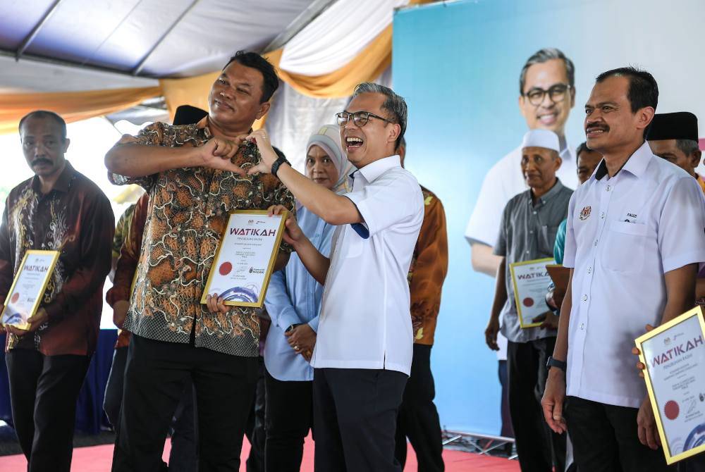 Fahmi (depan, kanan) membuat simbol 'mini love' bersama penerima Watikah Komuniti MADANI pada program Jiwa Madani di Kampung Seberang Ramai pada Sabtu. Foto Bernama