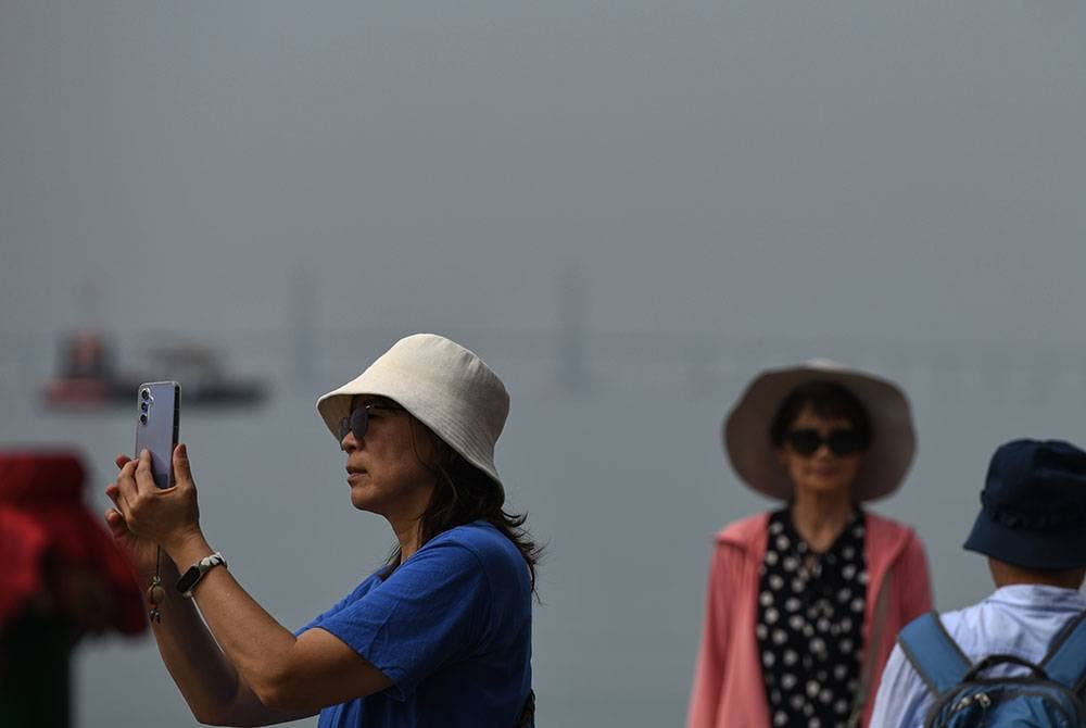 Para pelancong merakam gambar berlatarbelakang pemandangan Jambatan Pulau Pinang yang kelihatan kabur berikutan jerebu yang melanda di negeri ini.