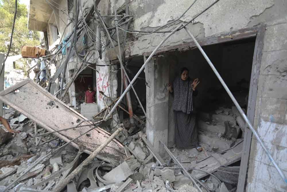 Seorang wanita Palestin berlindung di bawah bangunan yang separa musnah di Gaza.