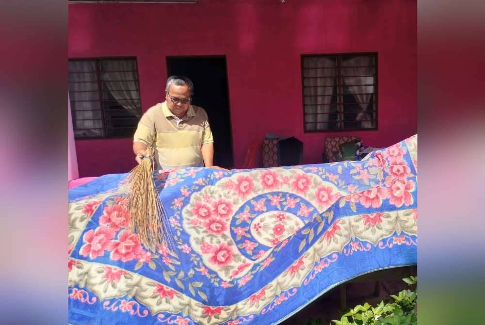 Raffee membersihkan karpet selepas rumah di Kampung Temenin Baru dilanda banjir kilat pada Sabtu.