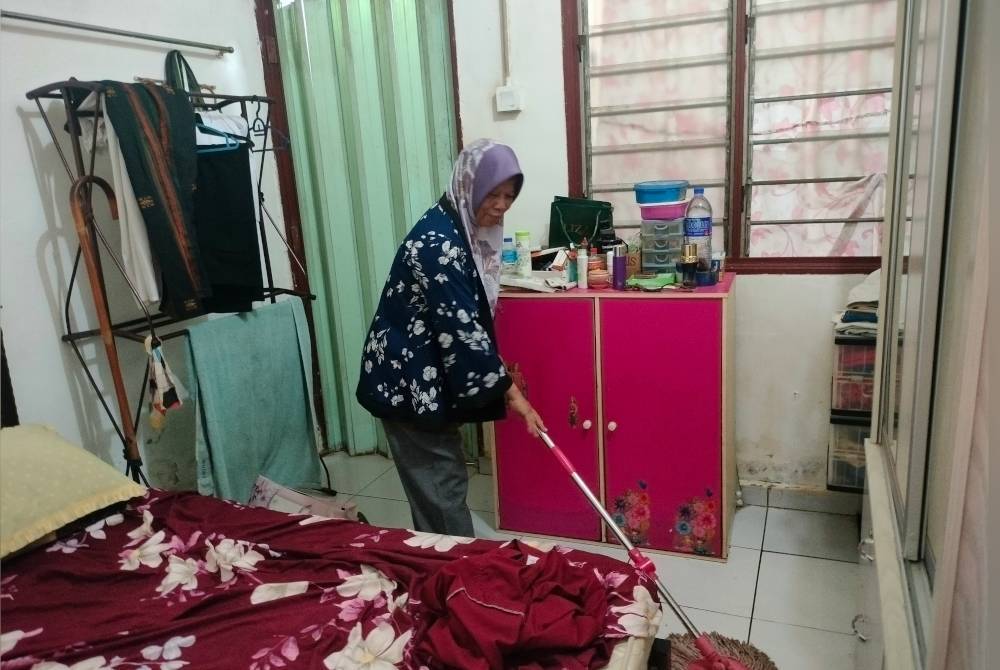 Hashimah mengemas rumahnya di Kampung Teminin Baru selepas banjir kilat melanda rumahnya pada Sabtu.