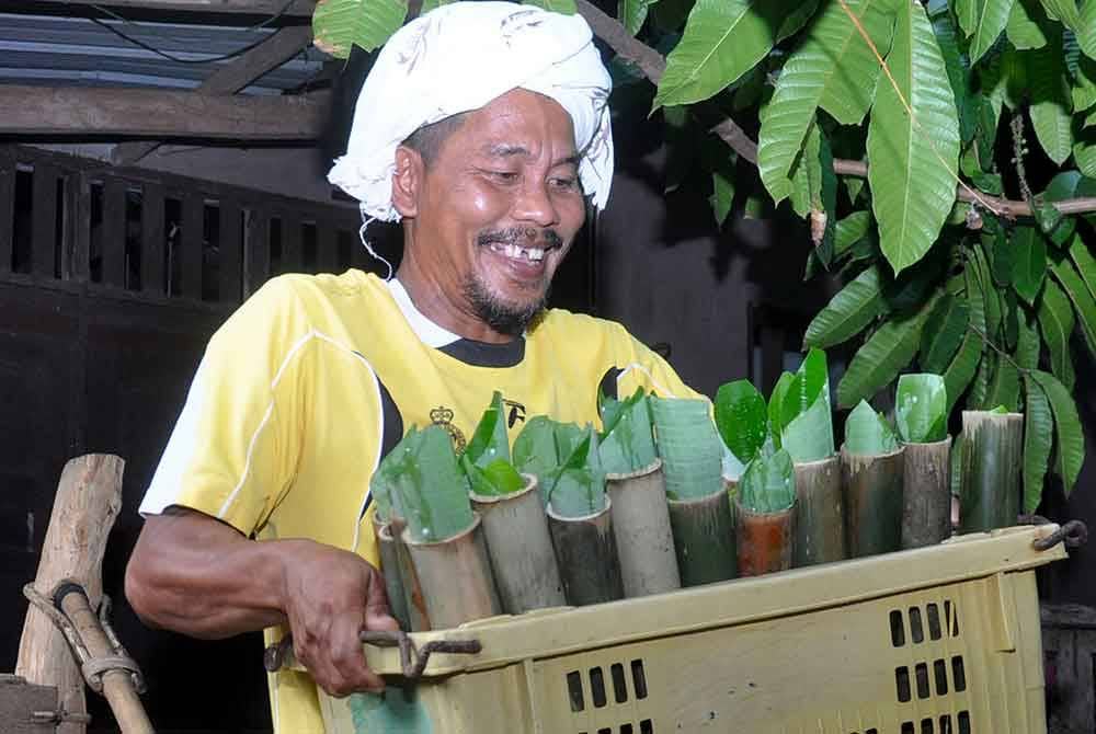 Peniaga lemang, Mohd Zailani Mohd Nor, 49, (kiri) mengangkat lemang untuk dibakar menggunakan dapur relau ciptaannya di rumahnya di Kampung Alor Belanga dekat Kampung Alor Keladi.