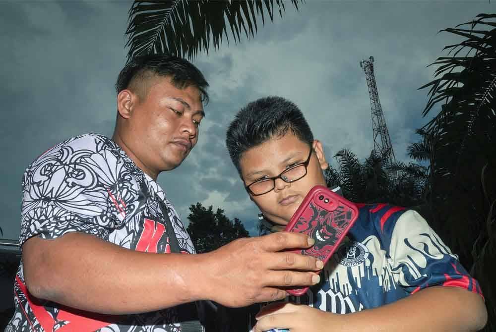 Penduduk kampung, Azrul Lau, 26, (kiri) bersama Yap Wei Kian, 11, melihat telefon pintar milik mereka yang telah mendapat sambungan internet di tapak projek POC Starlink di Menara Kampung Orang Asli, Kerling pada Khamis. Foto Bernama
