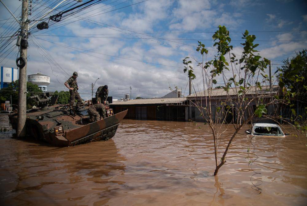Beberapa askar memerhati kenderaan mereka yang rosak akibat banjir di Eldorado do Sul.