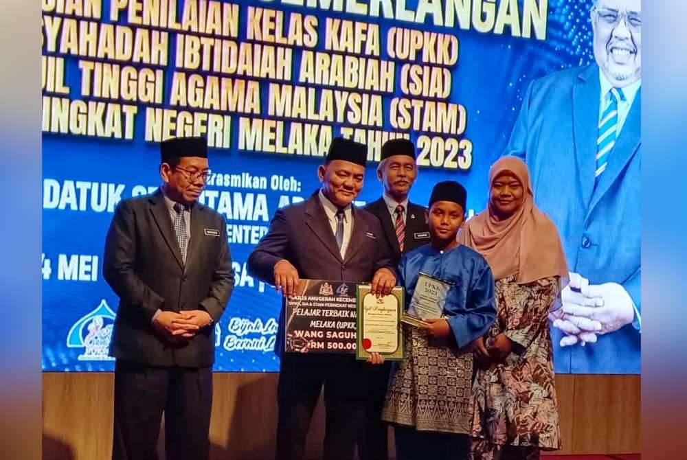 Badaruddin (kiri) dan Rahmad (dua dari kiri) ketika menyampaikan hadiah kepada pelajar terbaik UPKK 2023 peringkat negeri, Adam Nurfirdaus di sebuah hotel di Banda Hilir pada Selasa.