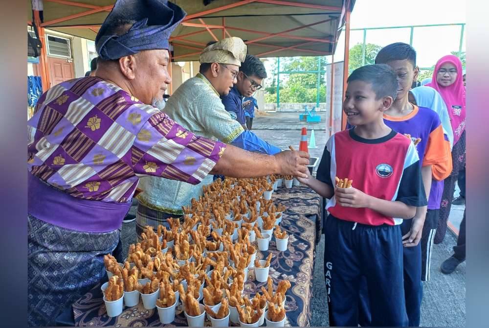 Mohd Alhamadi (kiri) dan Saiful (dua dari kiri) mengagihkan tempe goreng kepada murid pada program tempe sebagai pilihan tambahan bagi sumber protein dan galakan makan buah-buahan tempatan peringkat negeri di SK Padang Garuda pada Selasa.