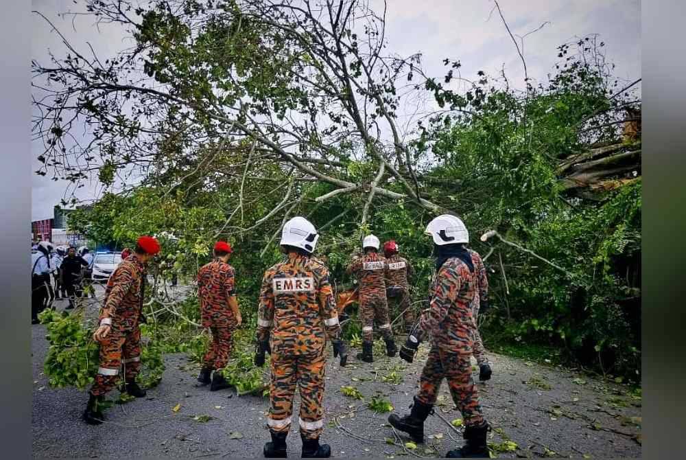 Anggota bomba melakukan kerja memotong pokok tumbang di Jalan Datuk Kumbar, di sini, pada Khamis.