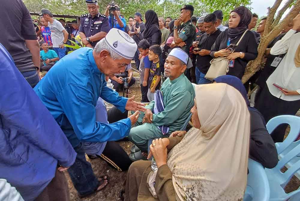 Ahmad Said (duduk) memeluk erat Jalur Gemilang di samping isterinya, Aini Mohd Sharif ketika di Tanah Perkuburan Islam Batu 8, Jalan Gambang pada Sabtu.