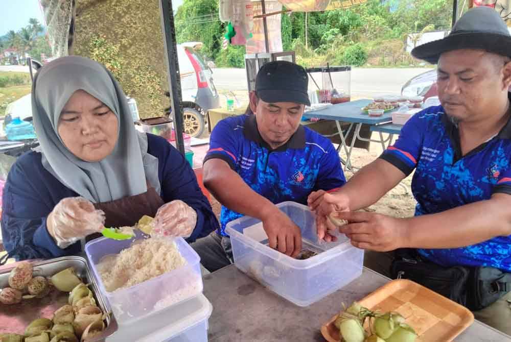 Zarina (kiri), Mohamad Jaya dan Kamal menyediakan lemang periuk kera untuk jualan di gerainya di Jalan Jelutong-Sokor, Kok Lanas.