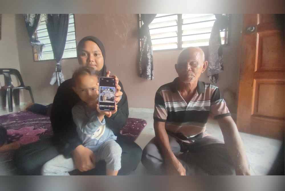 Ainul Mardiah ditemani ibu saudaranya, Hafyzoh dan datuknya, Abd Rahman menunjukkan gambar ibunya ketika ditemui di Kampung Sungai Mati, mukim Tobiar, pada Rabu.
