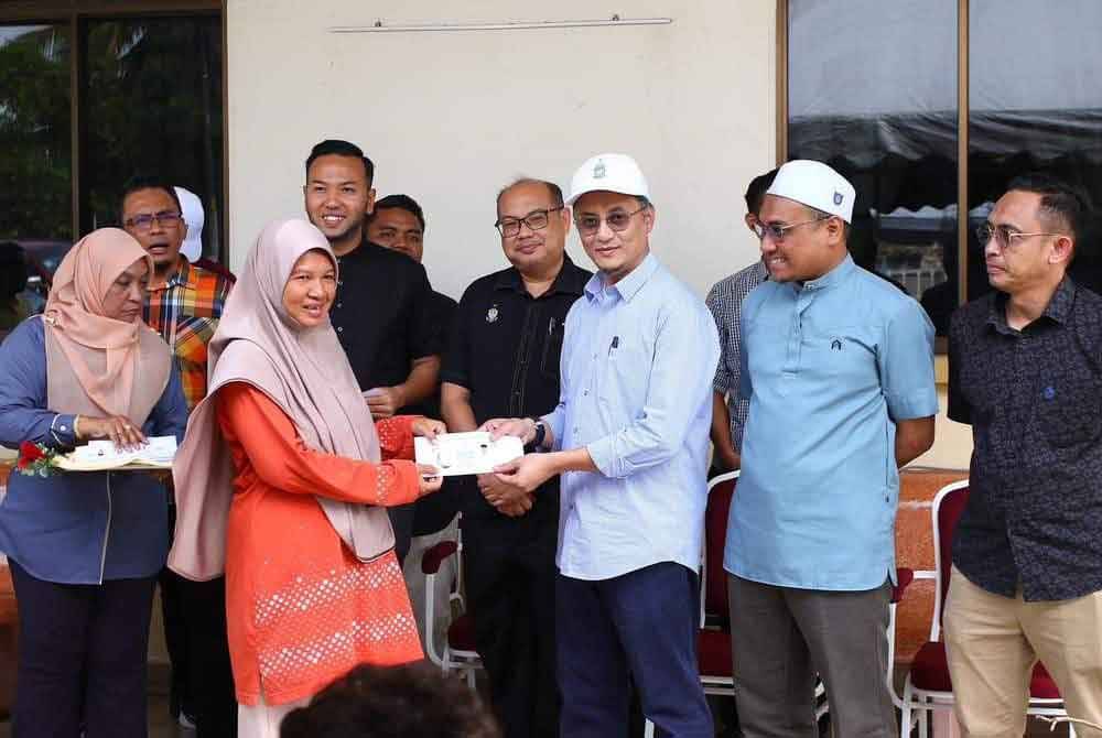 Mohamad (tiga dari kanan) menyampaikan sumbangan kepada salah seorang penerima skim bencana alam selepas rumah mereka terjejas dalam kejadian ribut baru-baru ini.