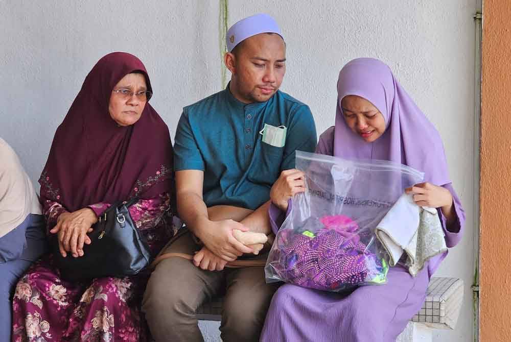 Nor Hashipah Ismail, 33, (kanan) tidak dapat menahan sebak ketika memegang pakaian terakhir yang dipakai kakaknya, Nor Aserah ketika menunggu di Jabatan Forensik, Hospital Taiping.
