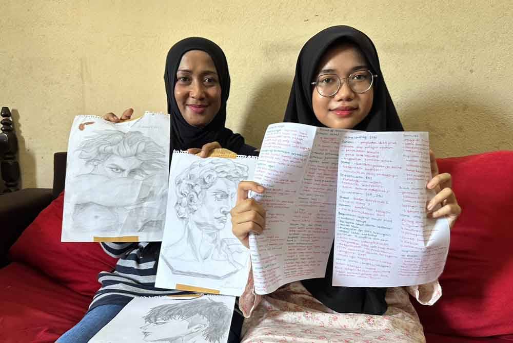Siti Bayu (kanan) menunjukkan nota-nota pembelajaran yang ditulisnya menggunakan pen berwarna merah dan lukisan dihasilkan.