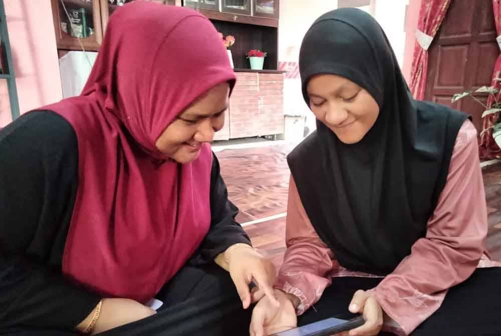 Siti Zaharah (kanan) menunjukkan keputusan SPM yang diterima kepada kakaknya, Nurkhairunnisa