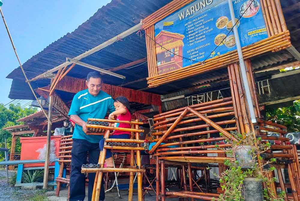 Abdul Rahman melayani cucunya yang duduk dalam kerusi bayi yang diperbuat daripada buluh di hadapan warungnya di sini.