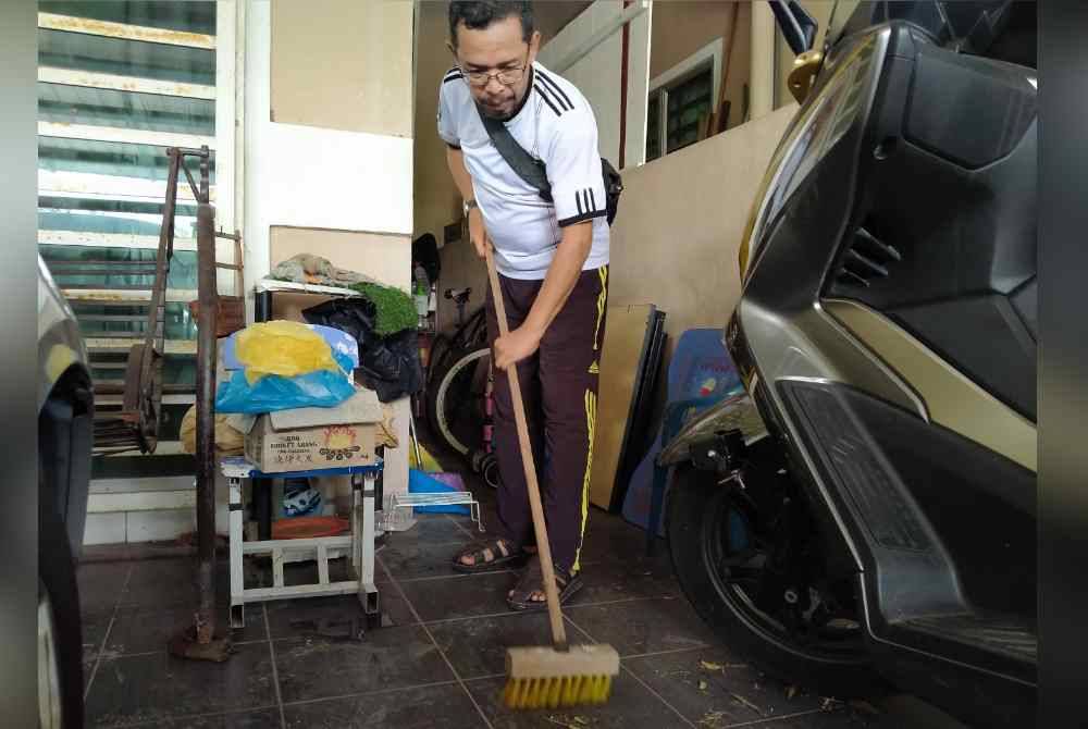 Burhanudin membersihkan sisa banjir lumpur di hadapan rumahnya yang berlaku baru-baru ini.