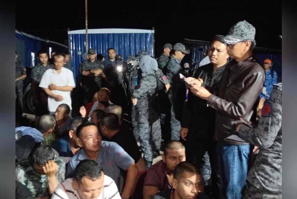 Jafri memeriksa dokumen warga asing yang ditahan di sebuah tapak pembinaan, di Pontian pada awal pagi Sabtu.