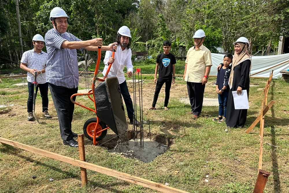 Husam (dua dari kiri) mencurah simen ke dalam tapak rumah milik Suhaini (kanan).