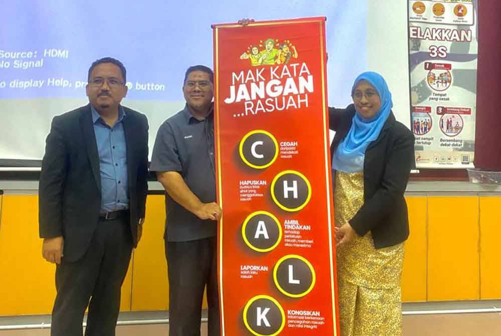 Nurhayati (kanan) menyerahkan gegantung kempen Rasuah Busters kepada Rozaidi (tengah) ketika program Jelajah Antirasuah MRSM di MRSM Taiping di sini pada Rabu.