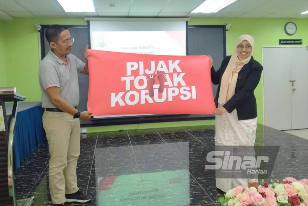 Nurhayati menyerahkan poster 'Pijak & Tolak Korupsi' kepada Nik Shahrullazwar sempena program Jelajah Antirasuah MRSM di MRSM Sultan Azlan Shah pada Khamis.