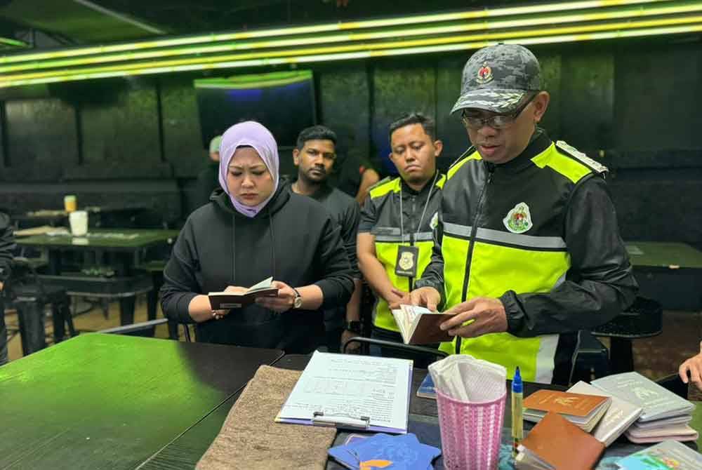 Khairrul Aminus (kanan) memeriksa dokuman pasport milik wanita asing dalam serbuan pusat hiburan di Leboh Gopeng, Klang pada Khamis.