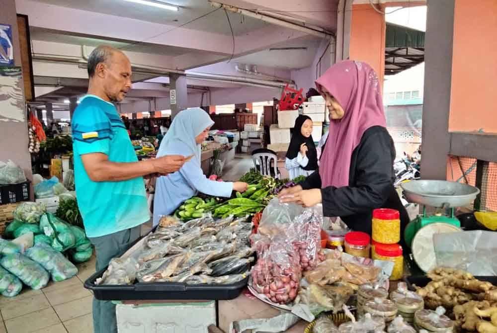 Rohani melayan pelanggan yang membeli ulam serta halia di gerainya di Pasar Siti Khadijah.