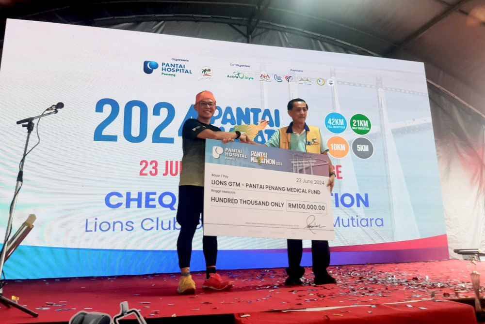 Wen Lek (kiri) menyerahkan replika cek RM100,000 kepada Penasihat Lions Club of George Town Mutiara, Datuk Khoo Kai Huat di Majlis Flag-Off Pantai Marathon 2024 pada Ahad.