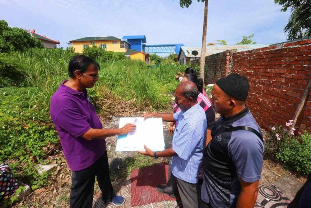 Mohd Rawi (kiri) melihat cadangan jalan berturap laluan keluar masuk yang sepatutnya dibina di kawasan penempatan Kampung Batu Baru Menglembu Timur, Ipoh.