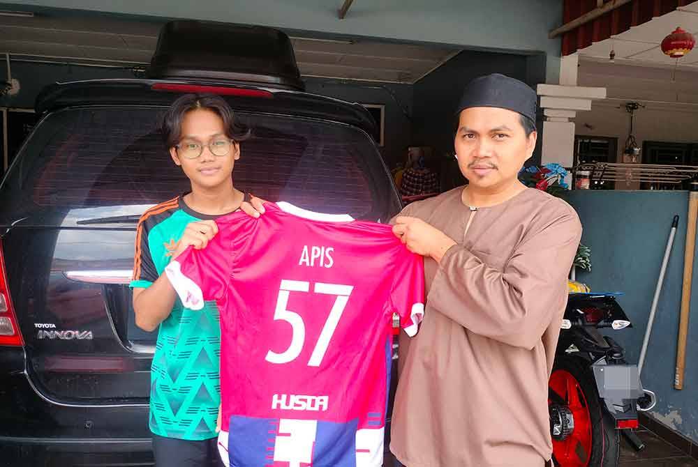 Abdul Halid (kanan) menunjukkan jersi bola yang dipakai Hafiz Fauzan ketika menyertai pertandingan bola sepak.