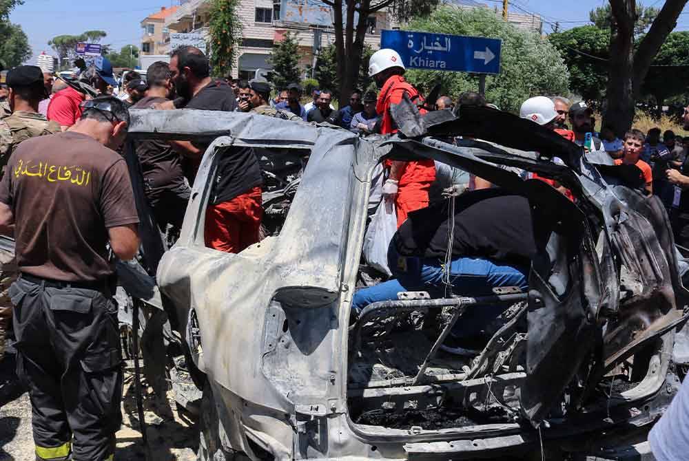 Anggota pasukan kecemasan menghampiri kereta yang hangus dibom tentera Israel di bandar al-Khiyara, barat Lubnan. - AFP