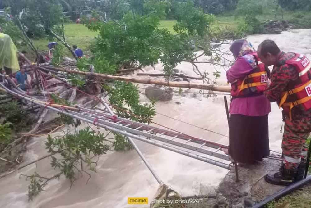 Anggota bomba membantu mangsa menyeberangi sungai selepas jambatan rosak akibat kepala air di Kampung Longob, Kota Marudu pada Isnin.