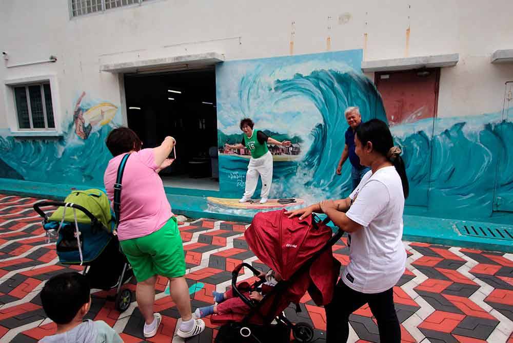 Seorang pengunjung beraksi seakan-akan meluncur ombak pada salah satu lukisan mural yang terdapat di Kuantan Art Street hari ini.