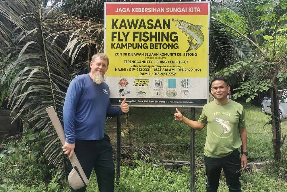 Christopher (kiri) dan Ramli menunjukkan papan tanda kawasan pancing layang di Sungai Berang, Hulu Terengganu.