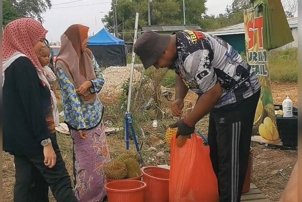 Zamadi (kanan) melayani pelanggan yang berkunjung ke gerai jualan durian di Seberang Takir.