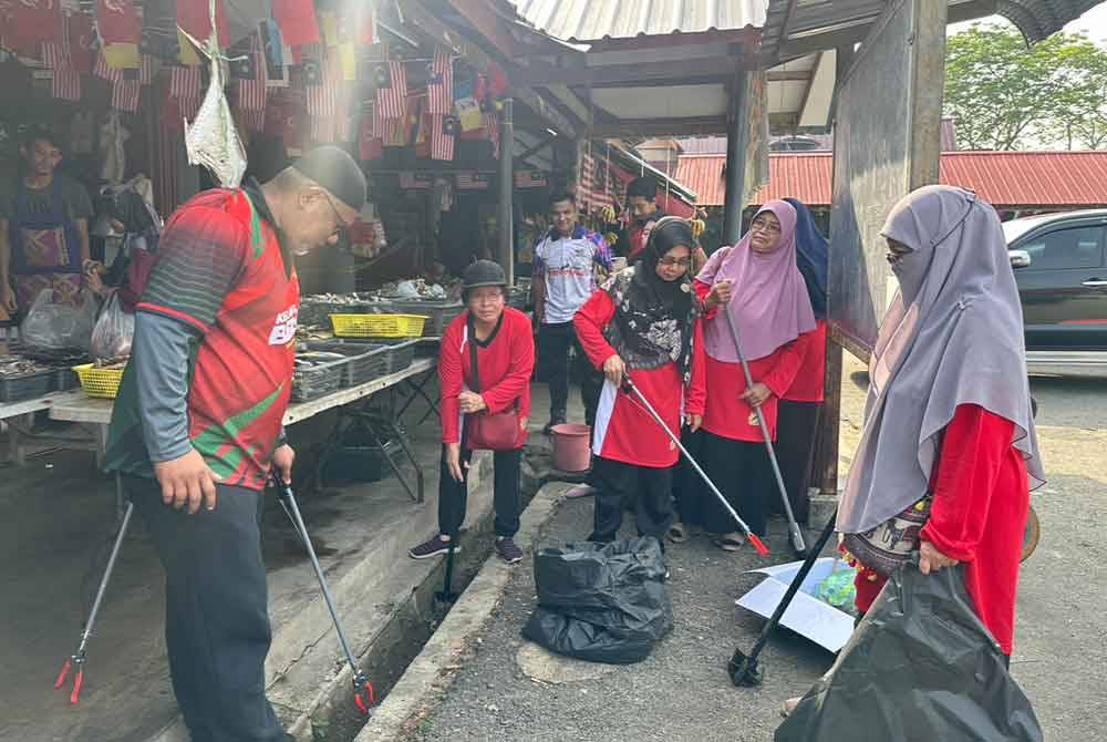 Peserta program bersama Zubir (kiri) membersihkan dan mengutip sampah di dalam longkang.