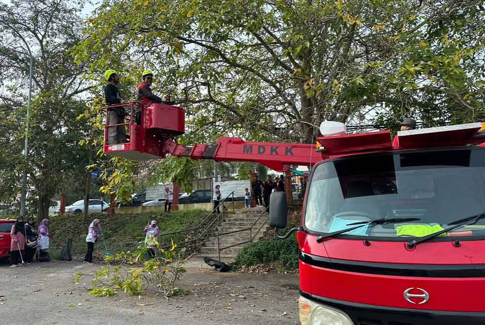 Zubir (kanan) menaiki jentera berat untuk memotong dahan pokok di sekitar kawasan pasar.