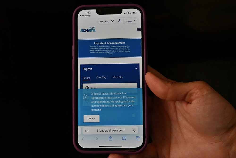 Seorang lelaki memegang telefon pintar yang memaparkan masalah teknikal berlaku dalam laman web syarikat penerbangan tambang murah Kuwait, Jazeera. - AFP