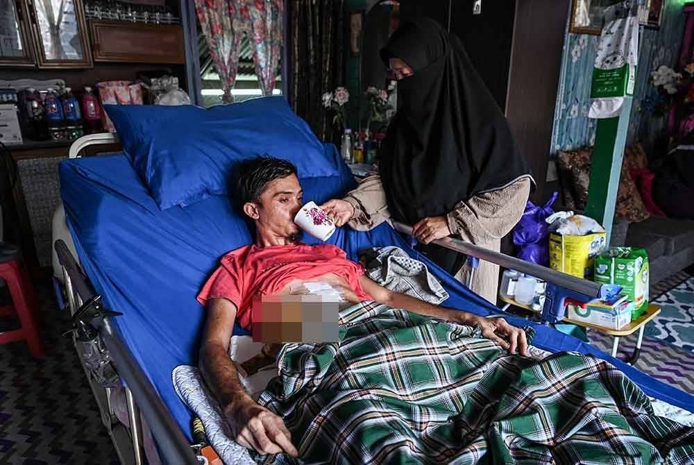 Ibu, Zaliha Chik, 61, (kiri) menguruskan anaknya, Abdul Mukmin yang terlantar ketika ditemui di Kampung Kuala Tepuh. Foto Bernama